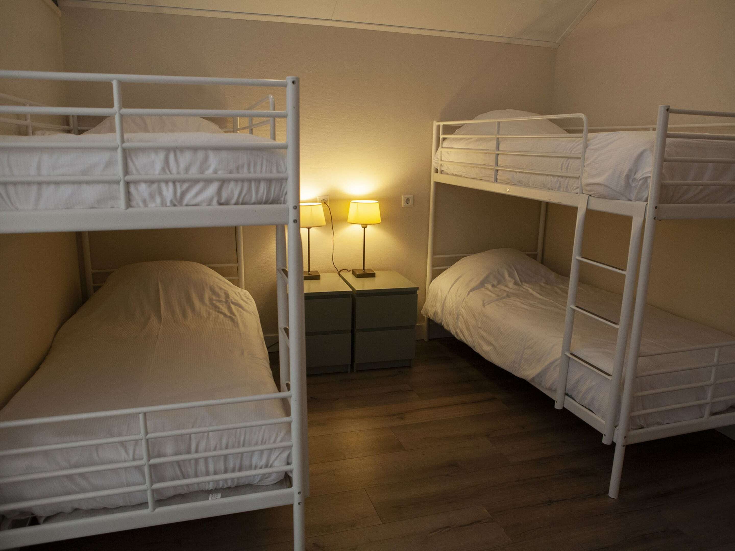Une chambre de dortoir avec des lits superposés, une table de chevet avec deux lampes et un plancher en bois.