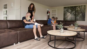 A modern living room with a brown leather sofa, two coffee tables, and a painting of a forest on the wall. - Villa in Netherlands With Private Pool (Voorthuizen)