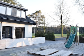 Una casa moderna con patio, un tobogán verde y un jardín cercado.