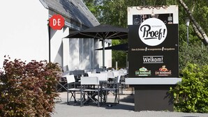 An outdoor seating area with tables and chairs, a sign for 'De Boshoek Restaurant', and a red 'DE' sign. - Villa in Netherlands With Private Pool (Voorthuizen)