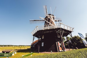Un moulin à vent traditionnel, doté d’une structure en bois et de pales métalliques, entouré d’une zone herbeuse et surplombé par un ciel dégagé.