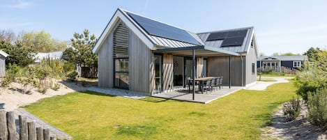 A modern house with a sloped roof, a patio with outdoor furniture, and a well-maintained lawn.