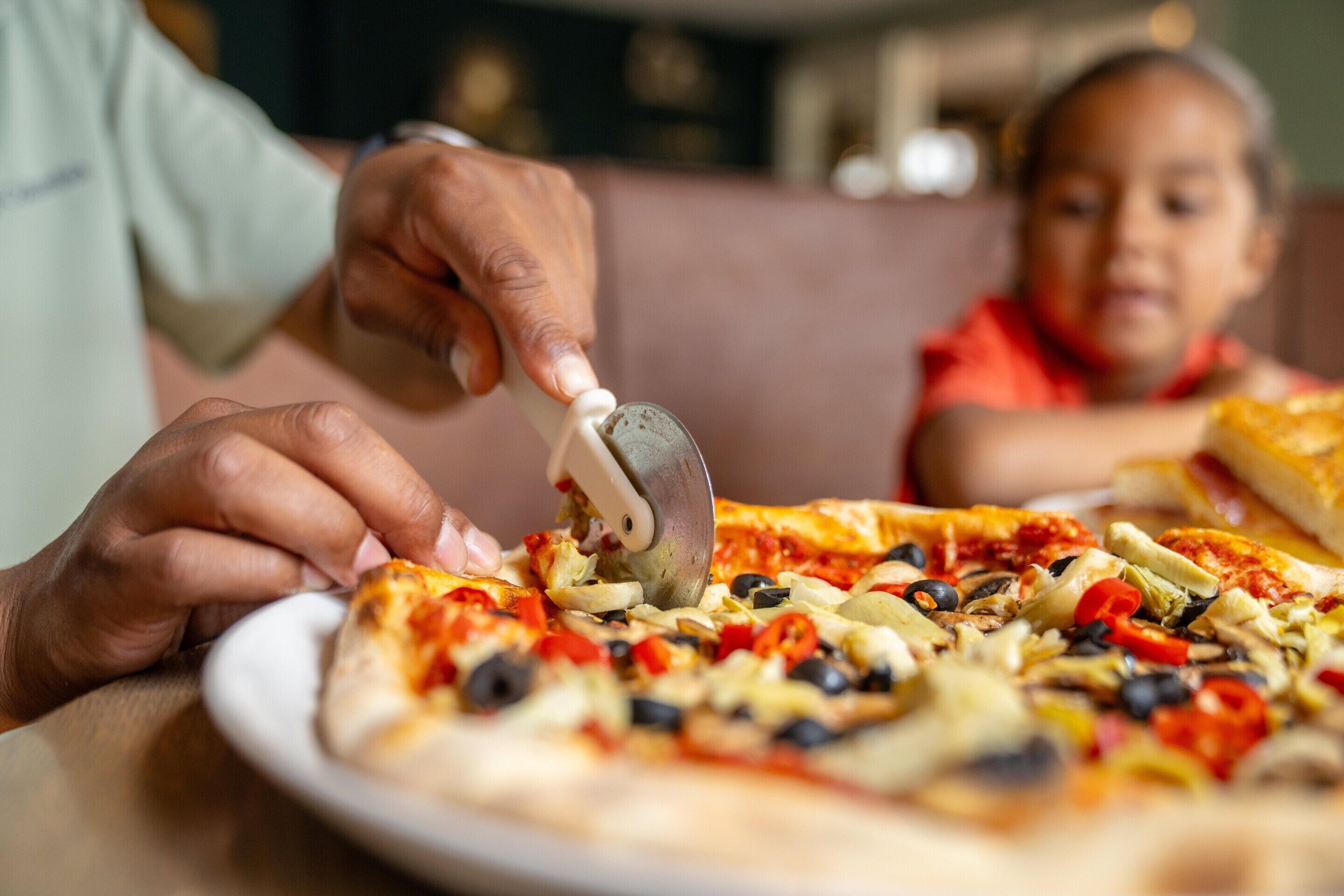 Una persona che taglia una pizza con un tagliapizza.