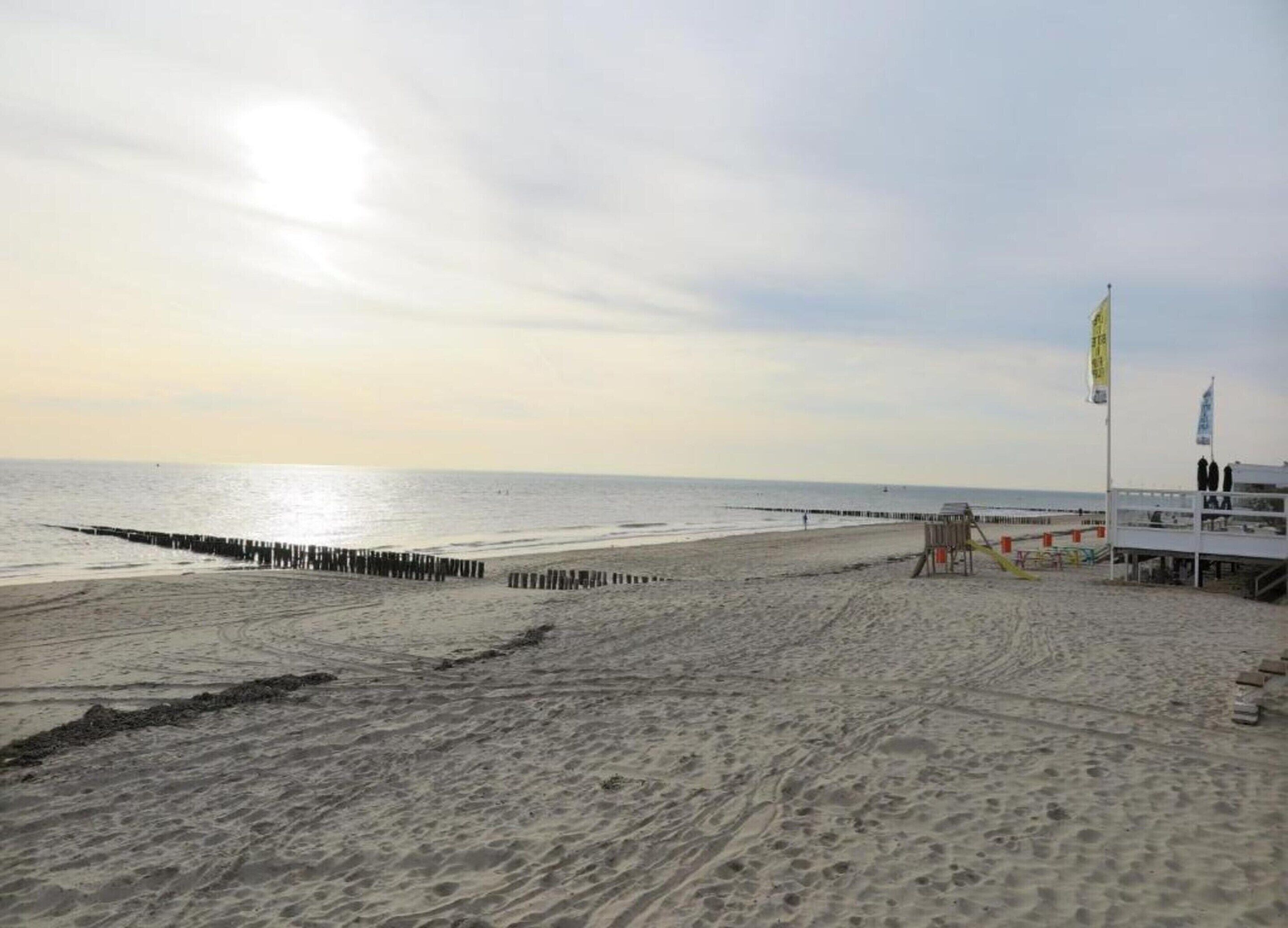 A beach with a wooden pier extending into the water, a lifeguard tower, and a clear sky.