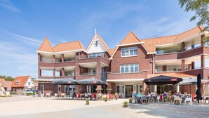 Een meerhoog gebouw met een rode pannendak, een terras en een overdekte patio met parasols.