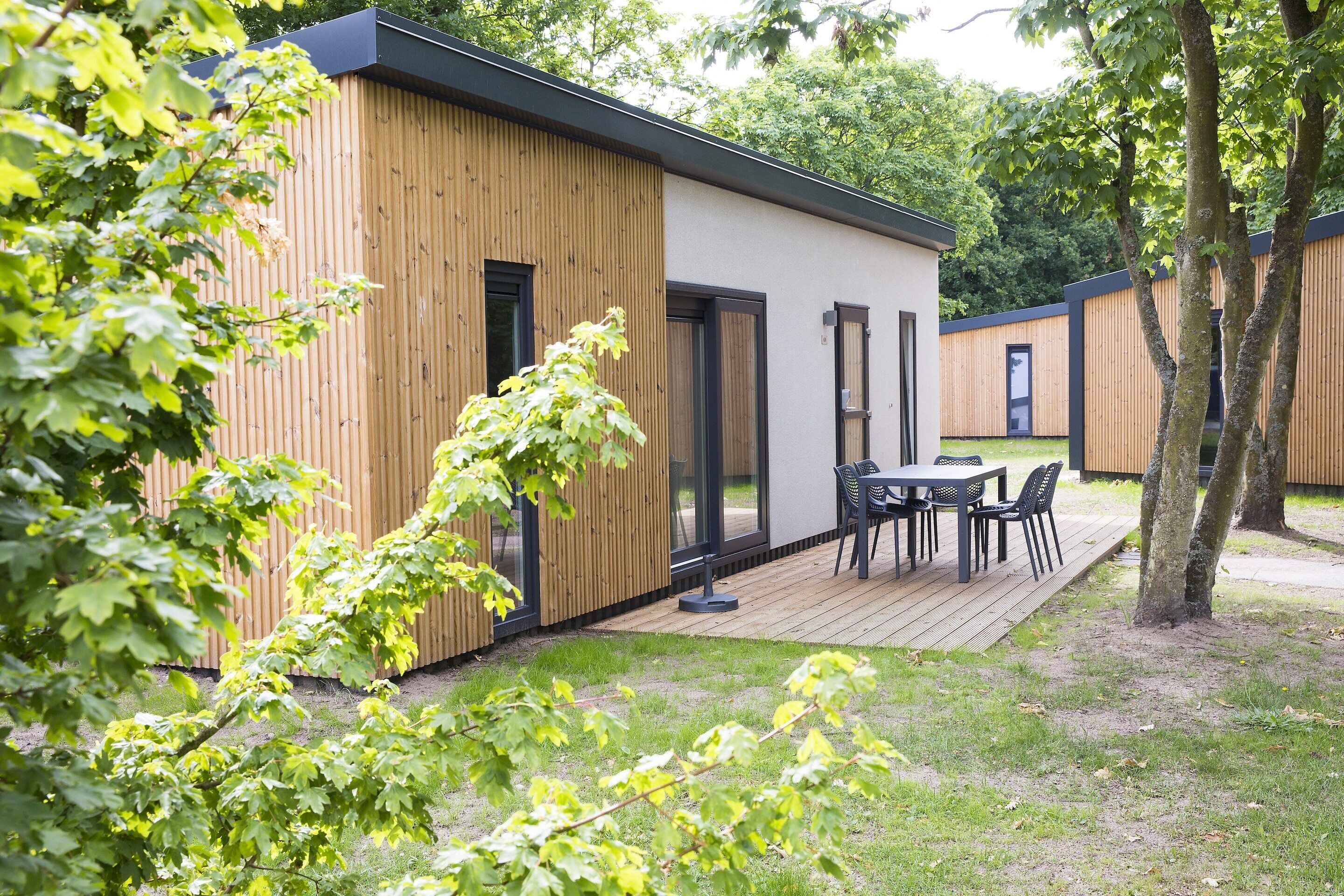A modern building with a wooden exterior, a deck with chairs, and a grassy area.