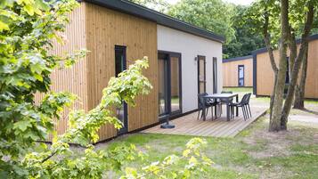 A modern building with a wooden exterior, a deck with chairs, and a grassy area.