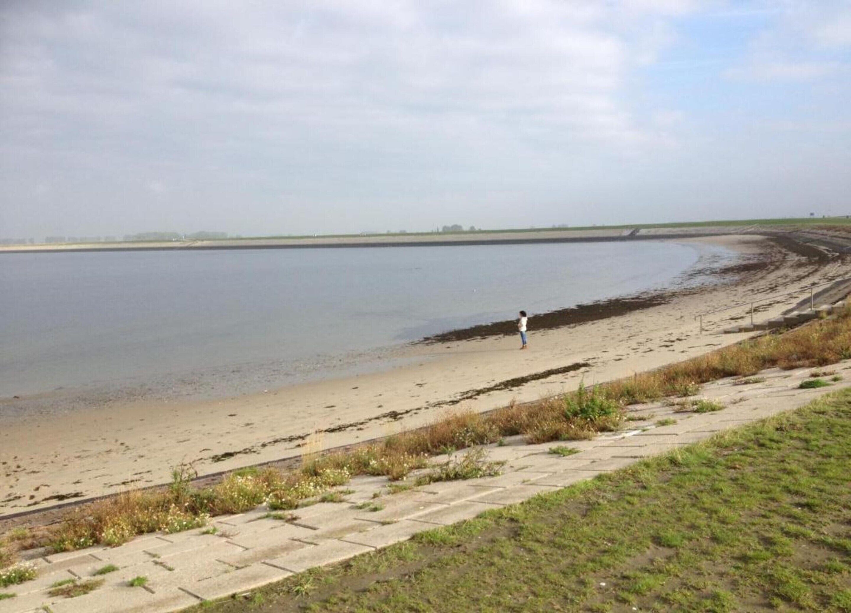 Un'ampia riva di fiume con una persona che cammina lungo il bordo.