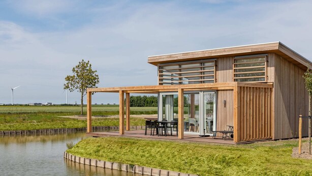 Una casa moderna con facciata in legno, ampie vetrate e una zona patio arredata.