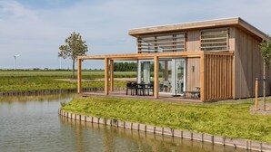 Una casa moderna con facciata in legno, un portico coperto con mobili da esterno e vista su un corpo d'acqua e turbine eoliche sullo sfondo.