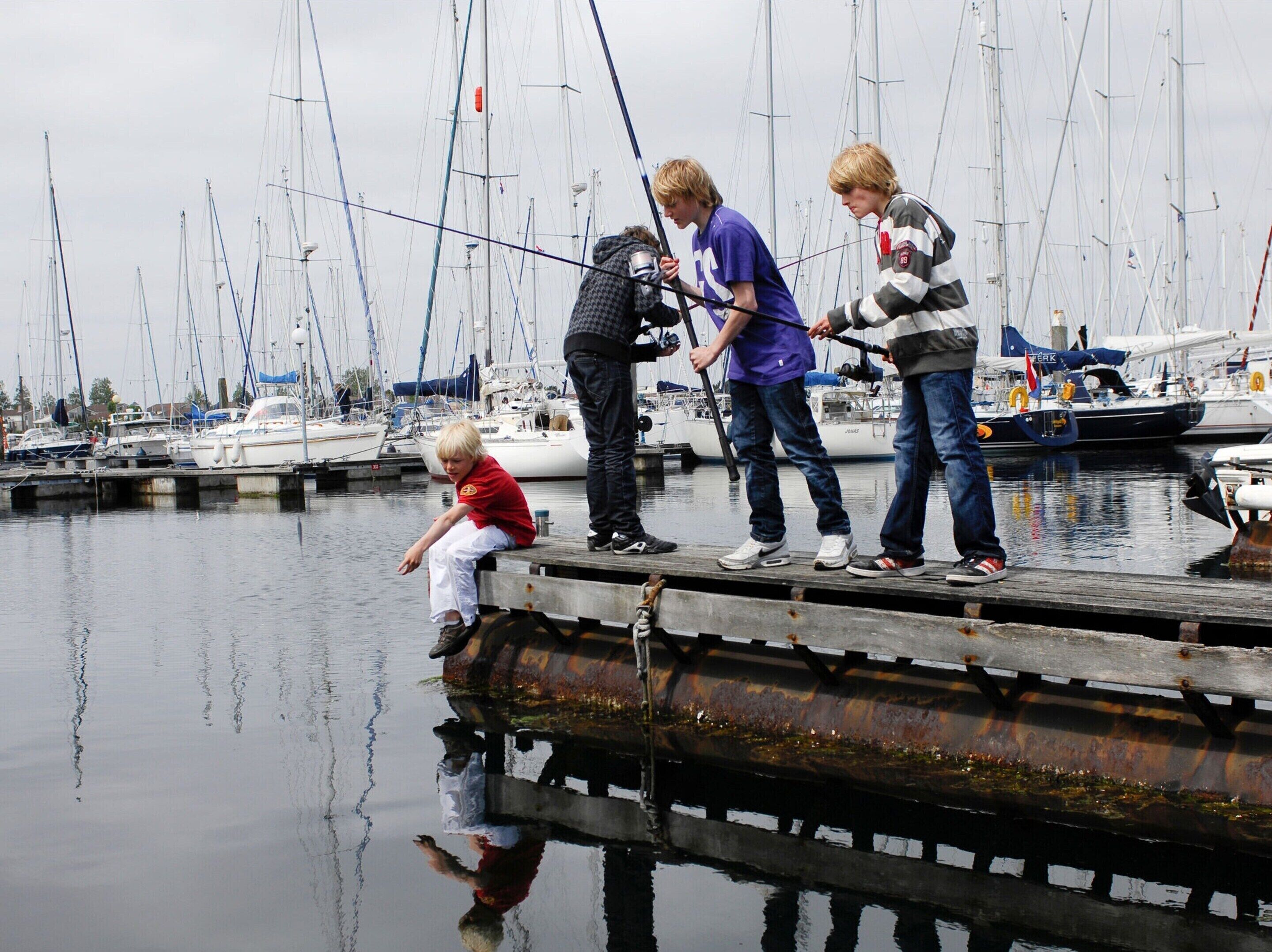 A marina with boats docked, a wooden pier, and people fishing.