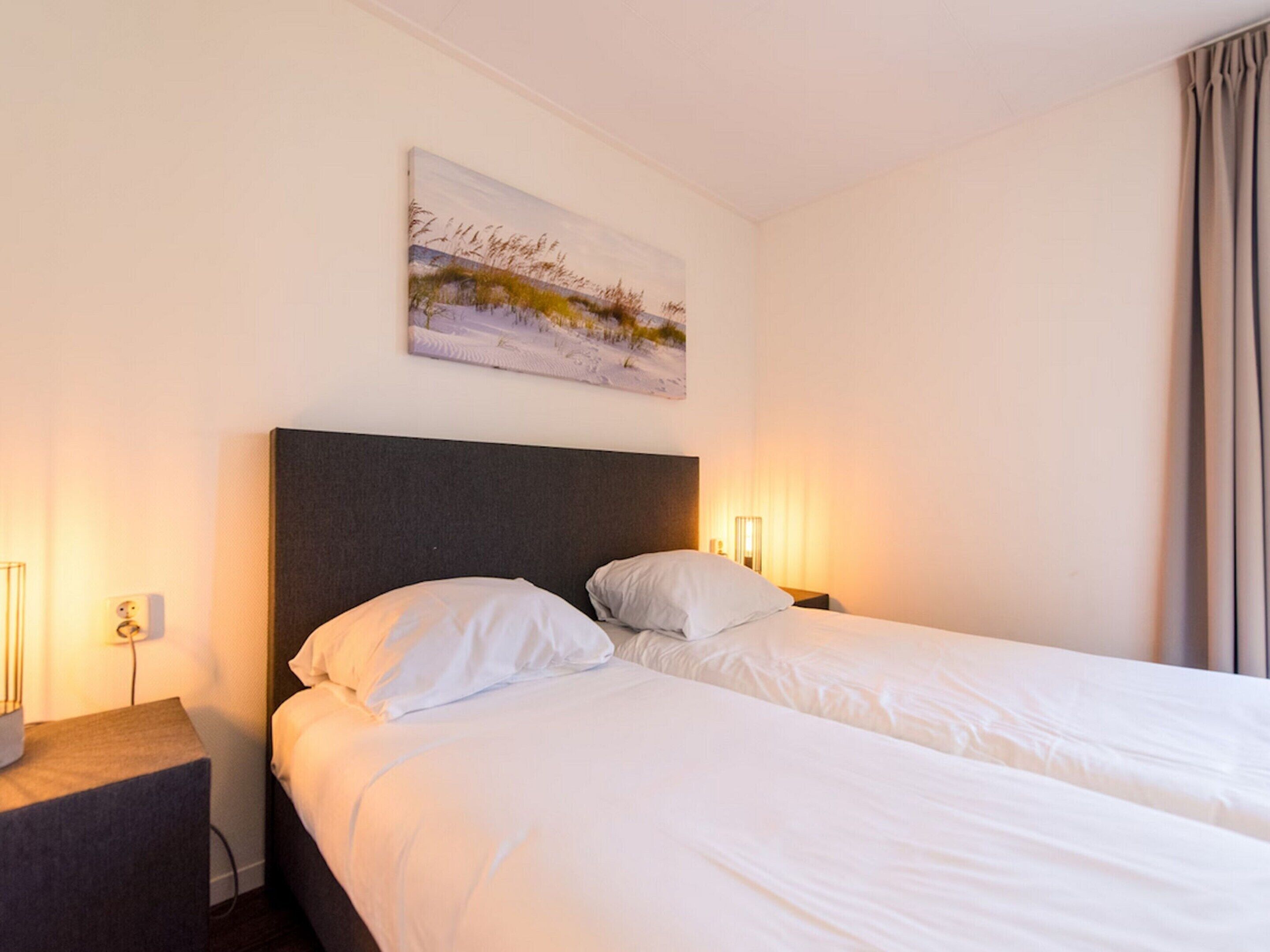 A hotel room with a large bed, two bedside tables, a nightstand, and a painting on the wall.
