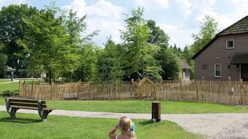 A grassy area with a wooden fence, a bench, and a building with a sloped roof.