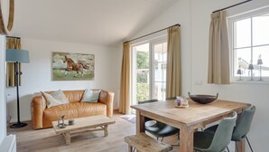 Una sala de estar acogedora con un sofá de cuero, una mesa de centro de madera y una mesa de comedor con sillas. Hay un cuadro en la pared y una ventana con cortinas.
