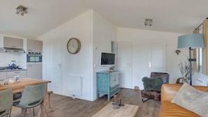 Un salón espacioso con una mesa de centro de madera, un sofá de cuero, una mesa de comedor con sillas, una cocina con electrodomésticos modernos y un reloj en la pared.
