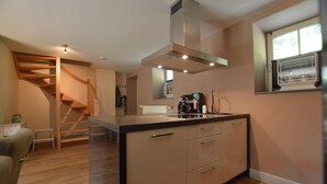Een moderne keuken met een centraal eiland, een houten trap en een raam met jaloezieën.