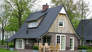 A two-story house with a steeply pitched roof, large windows, and a patio with outdoor furniture. - Stylish Retreat in Hellendoorn (Hellendoorn)