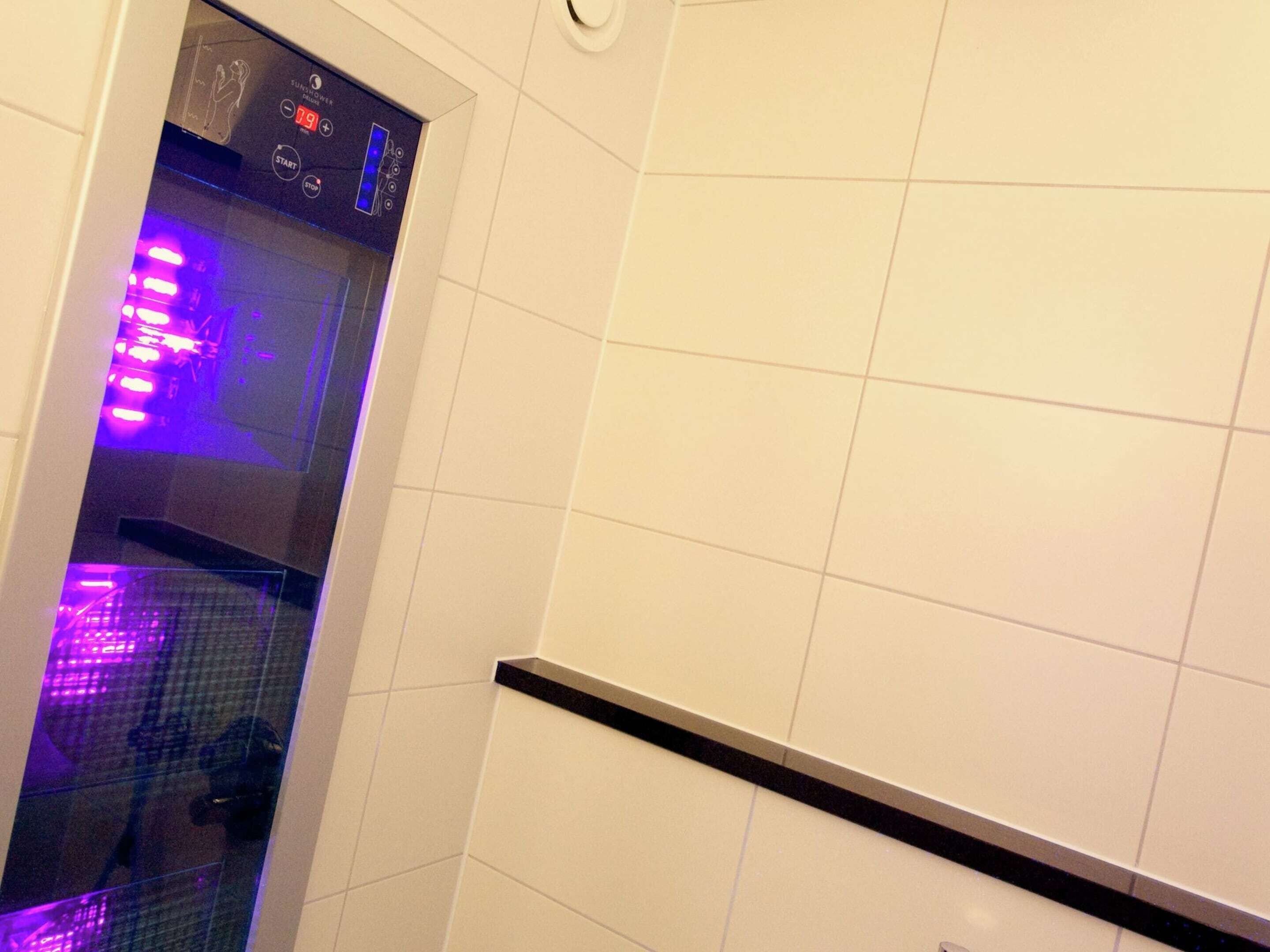 Une salle de bain avec des carreaux blancs, un comptoir noir et une douche en verre avec un éclairage violet.