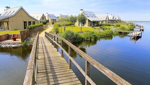A wooden dock leading to a row of buildings with sloped roofs, a calm water body, and a clear sky.