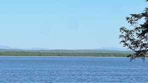 Three Adirondack chairs facing a lake with a forested shoreline and distant mountains. - Blue Spruce Lakefront Retreat - Recharge, reset, renew. (Alburgh)