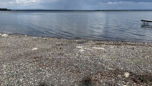 A pebbled beach with a wooden pier extending into calm water, under a partly cloudy sky. - Blue Spruce Lakefront Retreat - Recharge, reset, renew. (Alburgh)