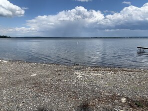 A pebbled beach with a wooden pier extending into calm water, under a partly cloudy sky.