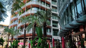 Un hotel de varios pisos con zonas de estar al aire libre, rodeado de exuberante vegetación y palmeras.