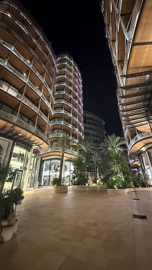 Une vue nocturne d’un hôtel à plusieurs étages, avec une cour intérieure agrémentée de palmiers et une façade illuminée.
