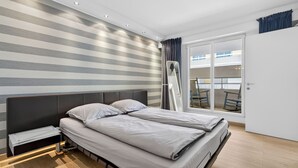 Un dormitorio moderno con una pared a rayas, una cama con cabecera, una mesita de noche y vistas a un balcón exterior.