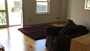Une pièce spacieuse dotée d’un plancher en bois, d’un canapé de couleur violet foncé, d’une armoire en bois et d’une grande fenêtre laissant entrer la lumière naturelle.