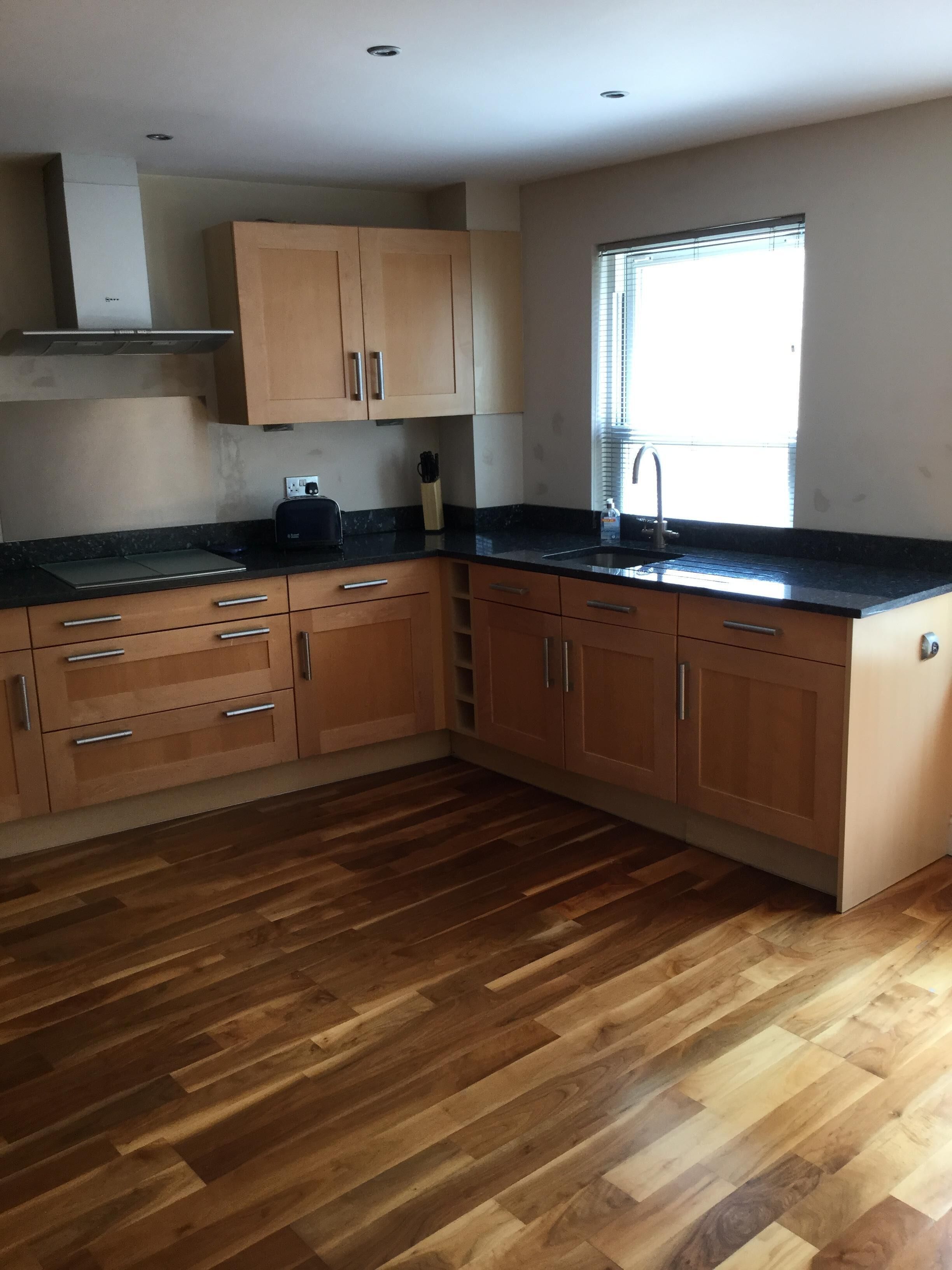 Una cocina con armarios de madera, encimera negra y una ventana con persianas.