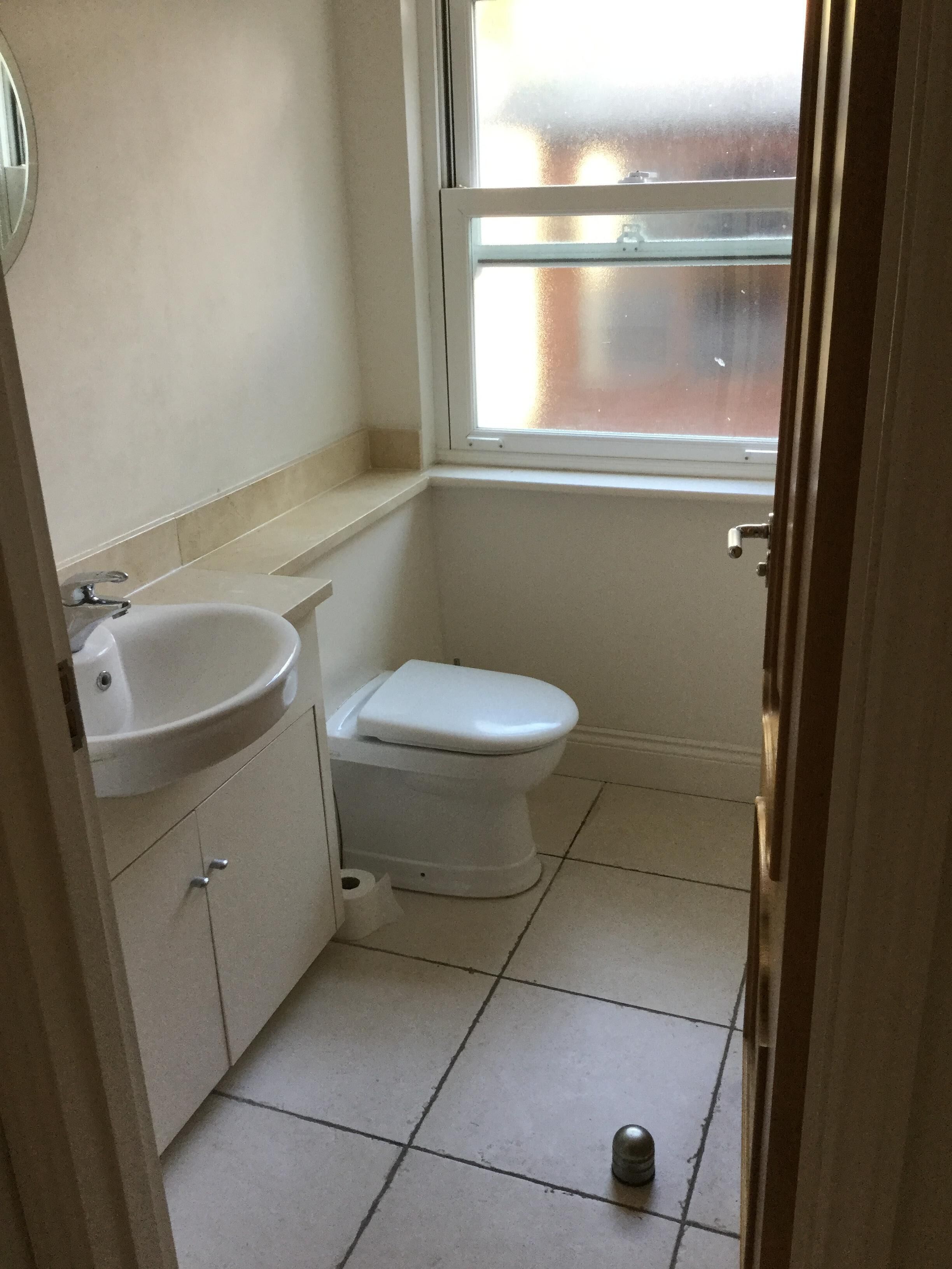 A small, clean bathroom with a white sink, toilet, and a window above the toilet.
