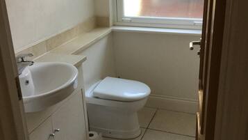 A small, clean bathroom with a white sink, toilet, and a window above the toilet.