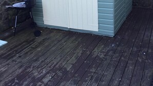 Un petit abri de plain-pied, avec une porte et une fenêtre blanches, situé sur une terrasse en bois, adossé à un mur de pierres.
