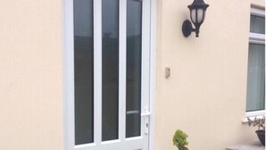 A building with a beige exterior, a white-framed window, and a black wall-mounted light fixture. - Ocean View Apartment (Grandes Rocques)