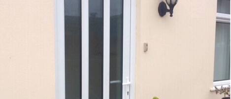 Um edifício com fachada bege, janela emoldurada por branco e luminária preta fixada na parede.