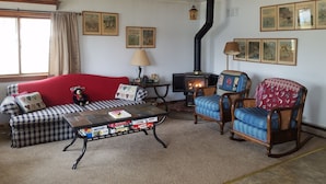 Una sala de estar acogedora con un sofá rojo, sillones azules, una mesa de centro con revistas, una chimenea y cuadros en las paredes.