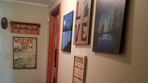 Un pasillo con un letrero de bienvenida, una cita enmarcada y una pintura de un lago.