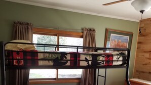 Una cama litera con una colcha a cuadros, un ventilador de techo y una ventana con cortinas.