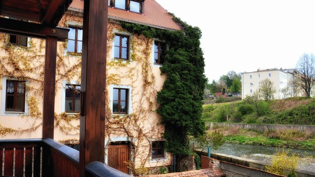 A building with ivy-covered walls, a stone bridge, and a river.