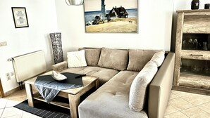 A living room with a beige sofa, a small wooden table, a remote control, and a framed picture of a lighthouse on the wall.