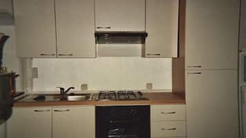 Une cuisine de taille réduite avec des meubles blancs, une cuisinière à gaz, un évier et un lave-vaisselle.
