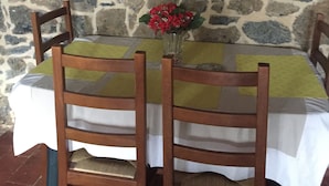 Pared de piedra con un adorno metálico sobre una mesa con mantel blanco, rodeada de sillas de madera.