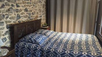 A bedroom with a stone wall, a wooden headboard, a patterned bedspread, and a curtain.