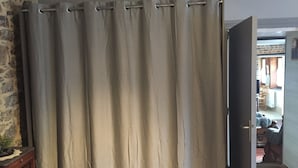 Una habitación con una cortina color crema, un aparador de madera y una vista parcial de un comedor al fondo.