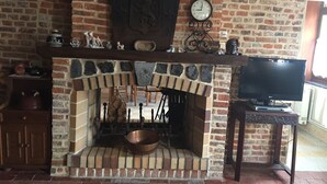 Una chimenea de ladrillo con un reloj encima, un televisor sobre un mueble a la derecha y un armario de madera a la izquierda.