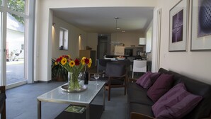 Un salon moderne avec une table basse en verre, un canapé agrémenté de coussins violets et un vase de fleurs.