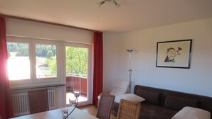 A living room with a brown sofa, a dining table with chairs, and a large window with a view of greenery. - Bright apartment (floor) with garden and balcony. Hegau, Lake Constance, Rhine Falls experience! (Tengen)
