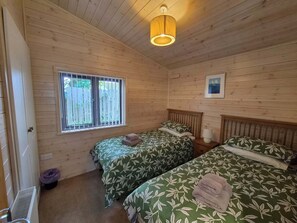Habitación tipo cabaña con dos camas, una ventana, un cuadro en la pared y una lámpara en el techo.