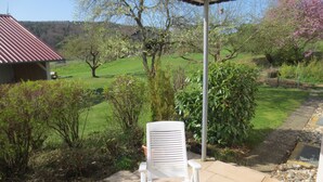 A patio with a white chair and table, overlooking a green landscape with trees and a building with a red roof. - Bright apartment (ground floor) with garden and terrace. Experience Hegau, Lake Constance, Rhine Falls! (Tengen)
